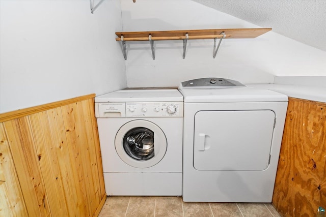 clothes washing area featuring light tile patterned floors, a textured ceiling, wooden walls, and washing machine and clothes dryer