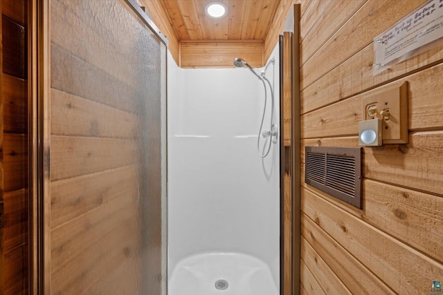 bathroom with wooden ceiling, a shower with shower door, and wooden walls