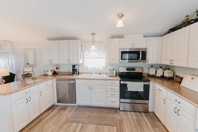 kitchen featuring white cabinets, sink, light hardwood / wood-style flooring, appliances with stainless steel finishes, and decorative light fixtures