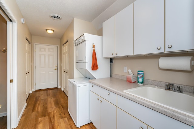 washroom featuring cabinets, sink, stacked washer and dryer, light wood-type flooring, and a textured ceiling