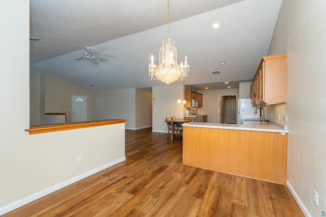 kitchen with kitchen peninsula, ceiling fan with notable chandelier, hardwood / wood-style flooring, and lofted ceiling