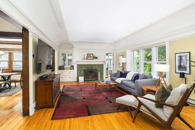 living room with a tiled fireplace, crown molding, and light wood-type flooring