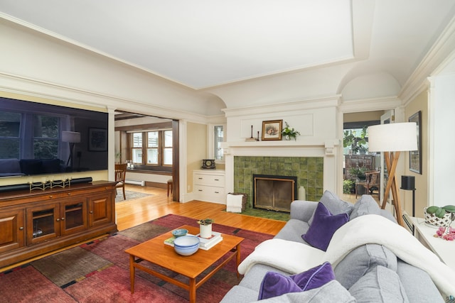 living room featuring wood-type flooring, baseboard heating, a healthy amount of sunlight, and a tiled fireplace