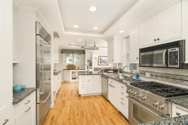 kitchen featuring kitchen peninsula, light hardwood / wood-style flooring, high quality appliances, dark stone countertops, and white cabinets