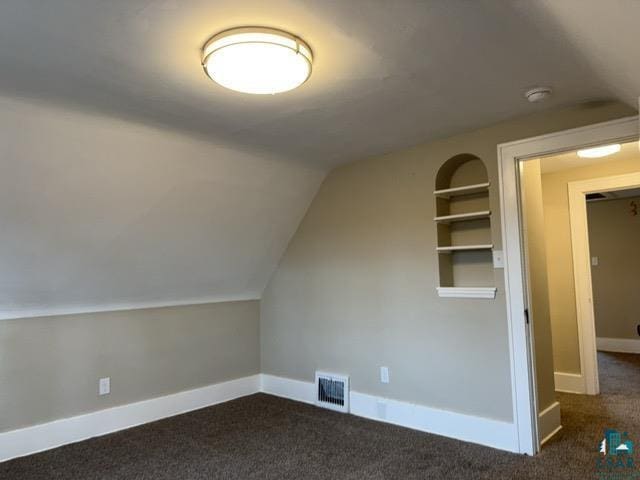 bonus room with built in shelves, dark carpet, and vaulted ceiling