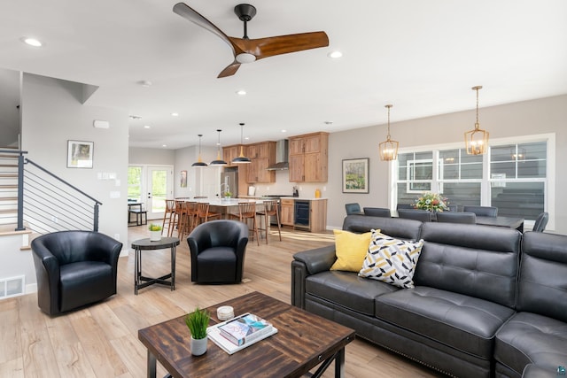 living room featuring wine cooler, light hardwood / wood-style floors, and ceiling fan with notable chandelier