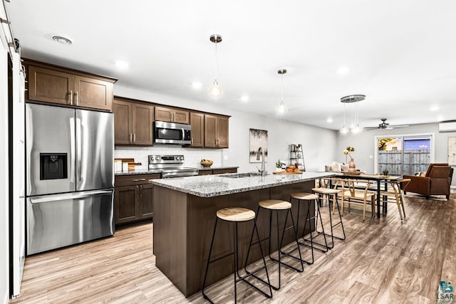 kitchen with ceiling fan, sink, light stone counters, a kitchen island with sink, and appliances with stainless steel finishes