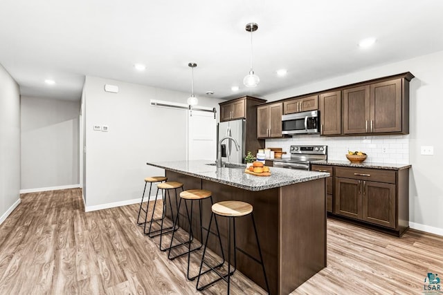 kitchen featuring light stone countertops, appliances with stainless steel finishes, backsplash, sink, and an island with sink