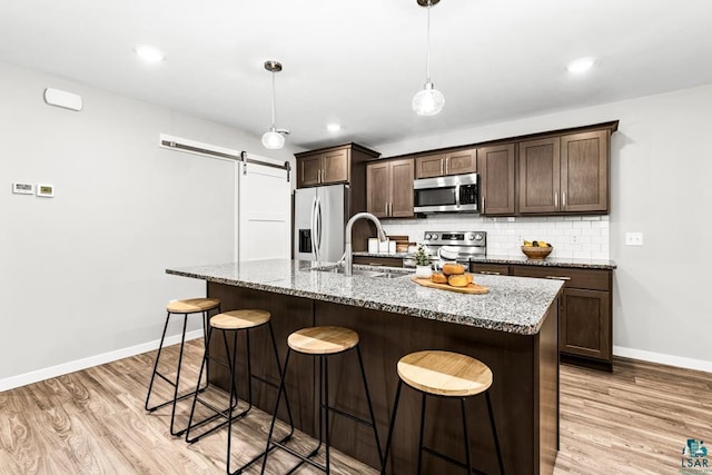 kitchen featuring backsplash, a kitchen island with sink, a barn door, light stone counters, and stainless steel appliances