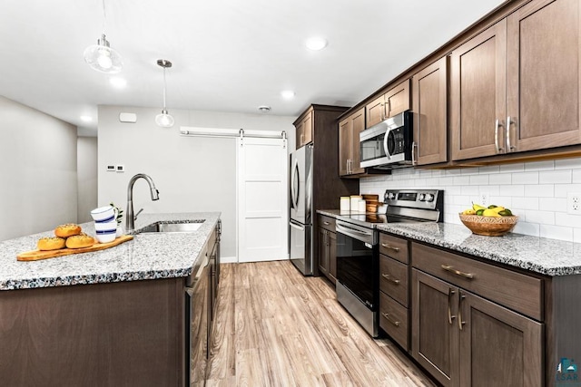 kitchen featuring appliances with stainless steel finishes, light stone counters, sink, a barn door, and decorative light fixtures