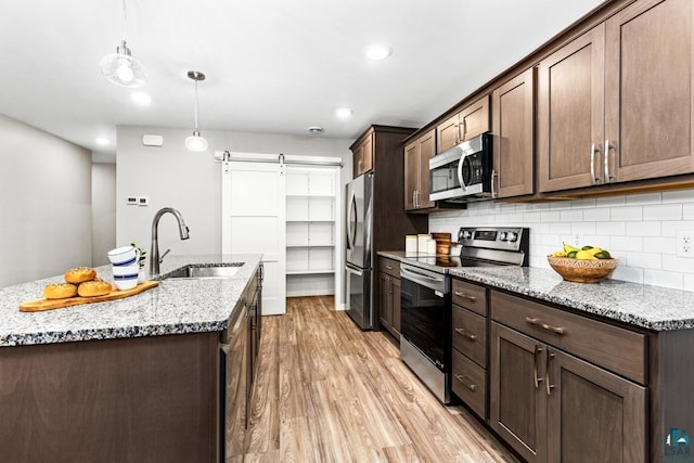 kitchen with light stone countertops, appliances with stainless steel finishes, backsplash, sink, and pendant lighting