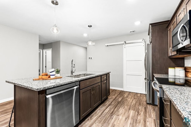 kitchen featuring sink, stainless steel appliances, a barn door, light stone counters, and a center island with sink