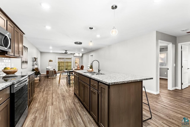 kitchen featuring appliances with stainless steel finishes, light stone counters, a kitchen island with sink, sink, and hanging light fixtures