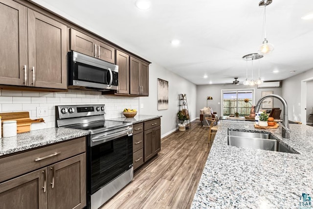 kitchen featuring light stone countertops, sink, stainless steel appliances, an AC wall unit, and dark brown cabinets