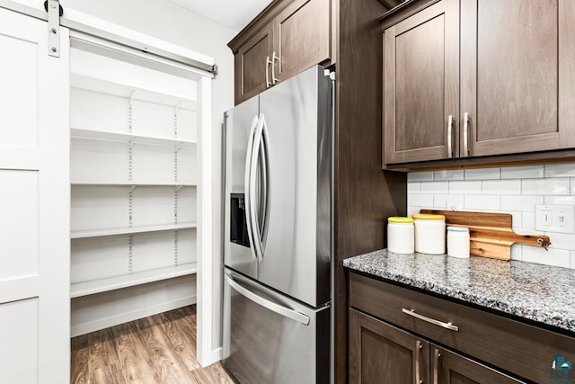 kitchen with dark brown cabinetry, light stone counters, stainless steel refrigerator with ice dispenser, backsplash, and light hardwood / wood-style floors