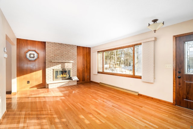 unfurnished living room featuring baseboard heating, wooden walls, hardwood / wood-style flooring, and a brick fireplace