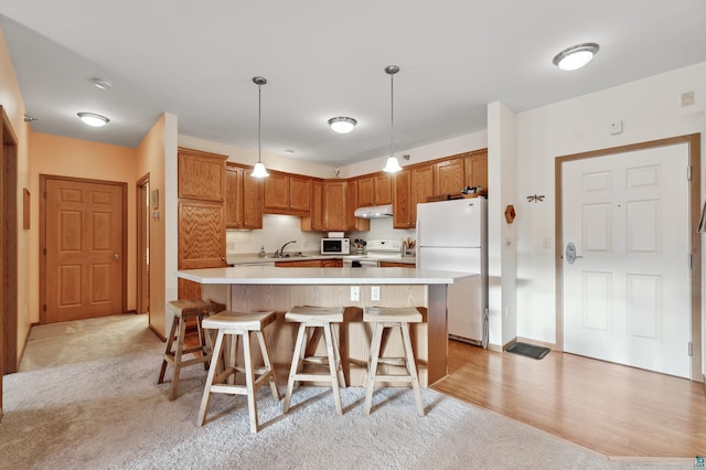 kitchen with white appliances, decorative light fixtures, a kitchen island, and light colored carpet