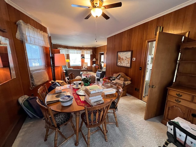 carpeted dining area featuring ceiling fan, wood walls, and ornamental molding