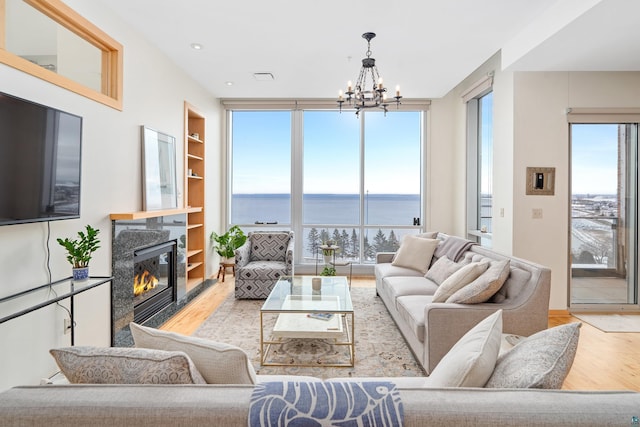 living room featuring a high end fireplace, a water view, light hardwood / wood-style floors, and a notable chandelier