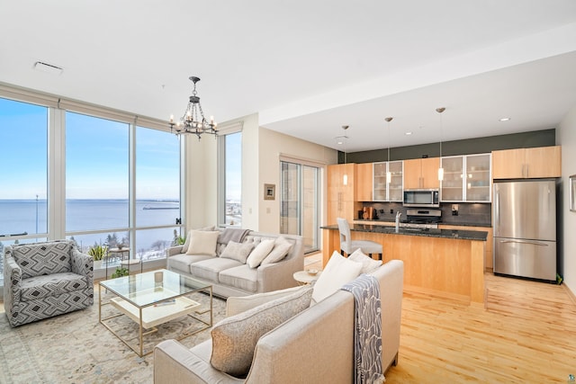 living room with a notable chandelier, light hardwood / wood-style floors, a water view, and a wall of windows