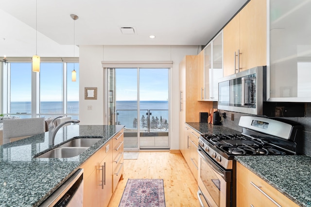 kitchen featuring sink, stainless steel appliances, decorative light fixtures, light brown cabinetry, and a water view