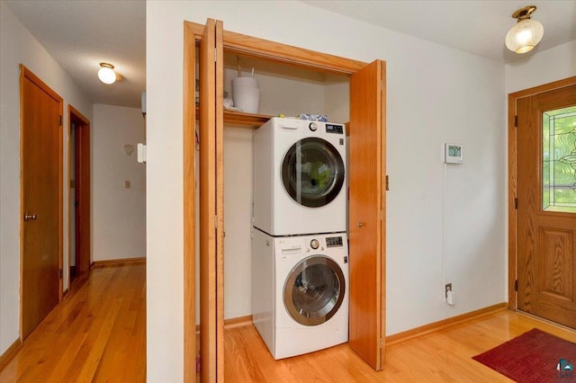 clothes washing area featuring a textured ceiling, stacked washing maching and dryer, and light hardwood / wood-style flooring