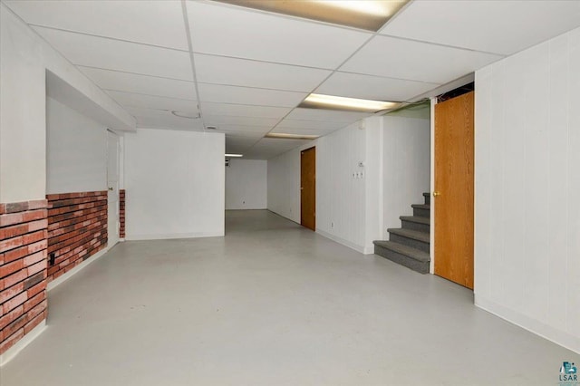 basement featuring a drop ceiling and wood walls