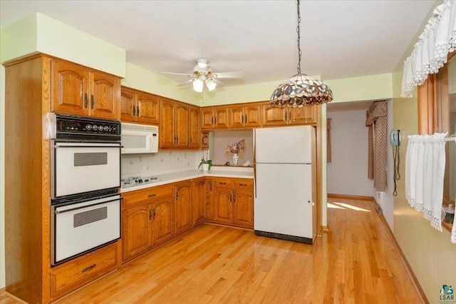 kitchen featuring white appliances, backsplash, hanging light fixtures, ceiling fan, and light wood-type flooring