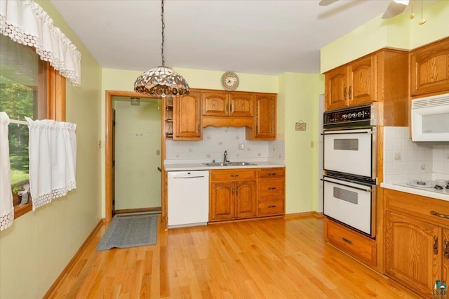 kitchen with white appliances, sink, light wood-type flooring, tasteful backsplash, and decorative light fixtures