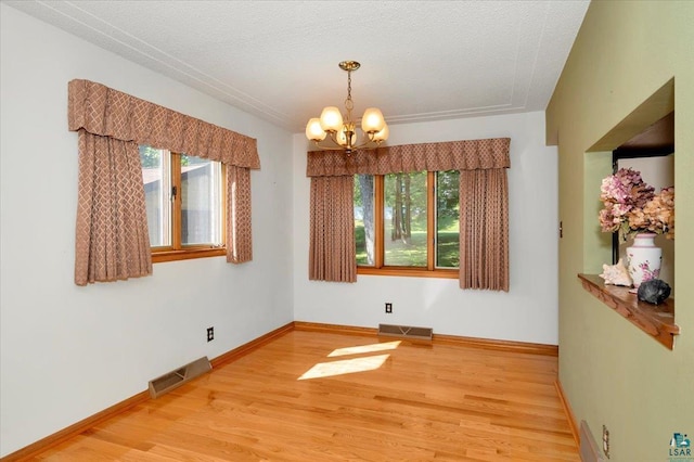 spare room with a chandelier, a textured ceiling, and wood-type flooring