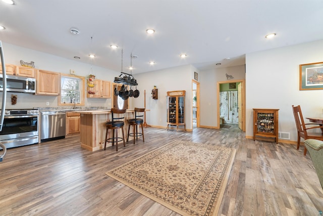 kitchen featuring hardwood / wood-style flooring, light brown cabinetry, a kitchen island, a kitchen bar, and stainless steel appliances