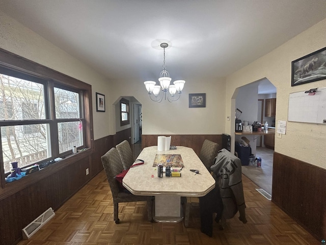 dining area with dark parquet flooring, an inviting chandelier, and wood walls