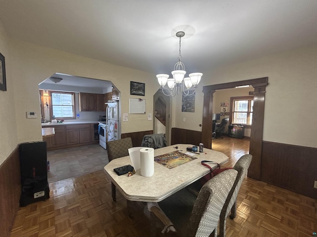 dining room with dark parquet flooring, an inviting chandelier, wooden walls, and decorative columns