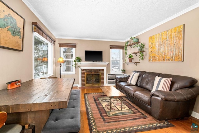 living room with a brick fireplace, a textured ceiling, crown molding, and wood-type flooring