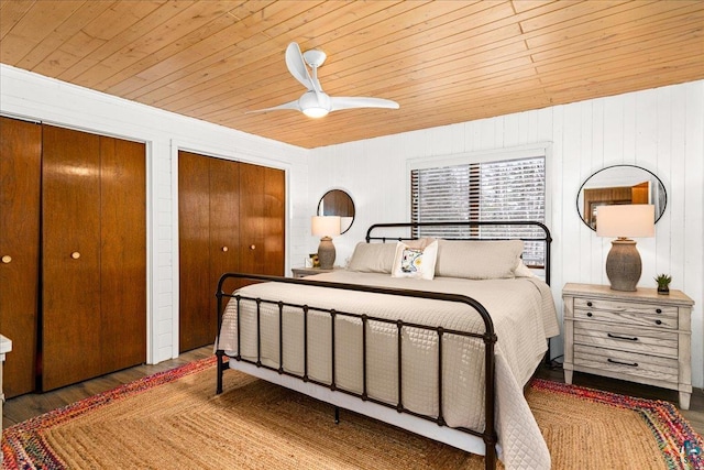 bedroom featuring wood ceiling, hardwood / wood-style floors, ceiling fan, multiple closets, and wooden walls