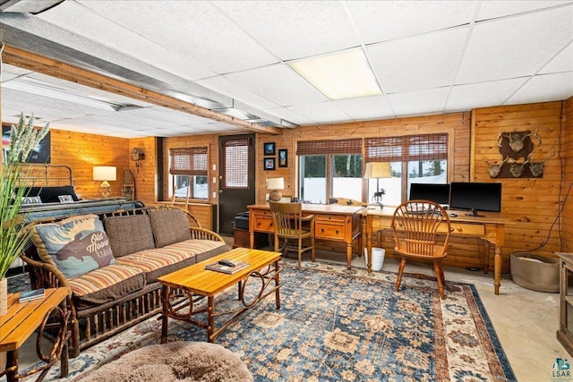 living room featuring concrete flooring, wooden walls, and a drop ceiling