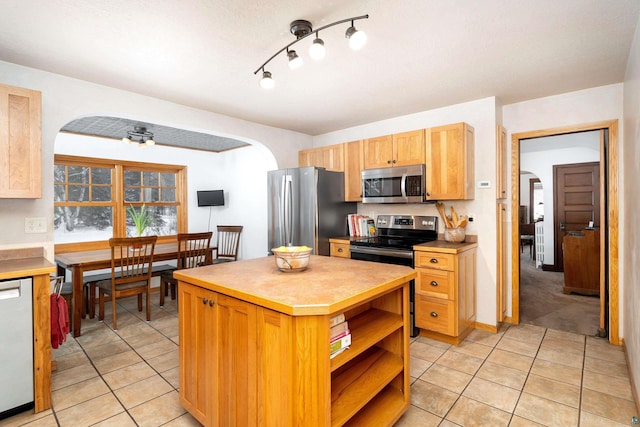 kitchen with light tile patterned floors, appliances with stainless steel finishes, light brown cabinets, and a center island