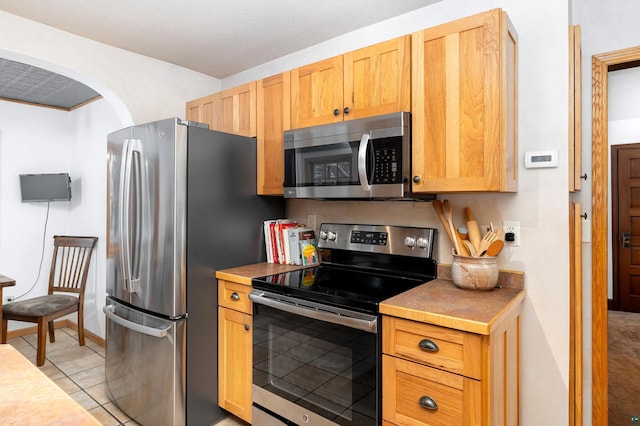 kitchen with light brown cabinetry, light tile patterned floors, and appliances with stainless steel finishes