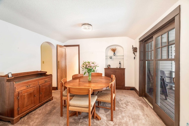 dining area featuring a textured ceiling, lofted ceiling, light colored carpet, and built in shelves