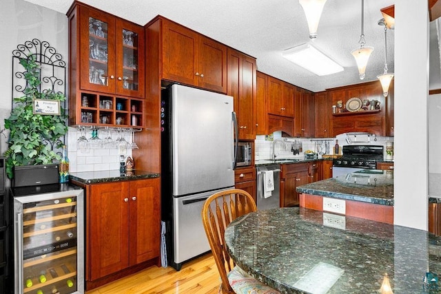 kitchen with a textured ceiling, appliances with stainless steel finishes, decorative light fixtures, wine cooler, and sink