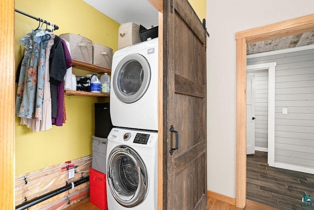 laundry room featuring stacked washing maching and dryer, dark hardwood / wood-style floors, and a barn door