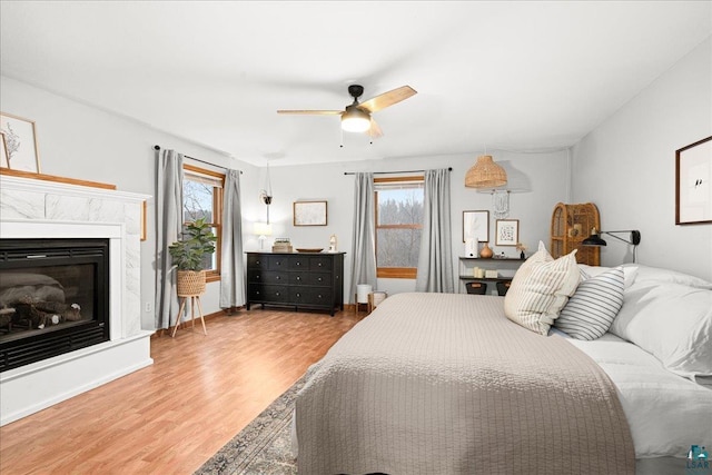 bedroom with ceiling fan, wood-type flooring, a high end fireplace, and multiple windows