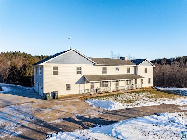 snow covered rear of property with covered porch and a garage