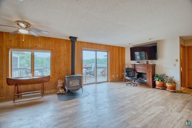 living room featuring ceiling fan, wooden walls, a wood stove, and a textured ceiling