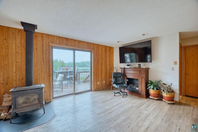 home office with a wood stove, a textured ceiling, light wood-type flooring, and wooden walls