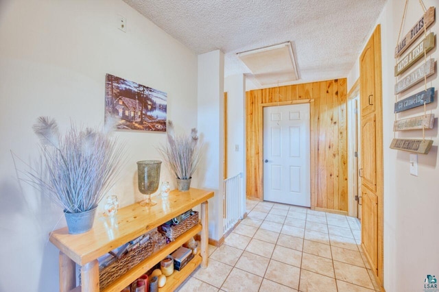 hall featuring a textured ceiling, light tile patterned floors, and wood walls