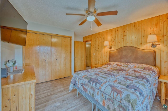 bedroom featuring ceiling fan, wood walls, light hardwood / wood-style flooring, a textured ceiling, and a closet