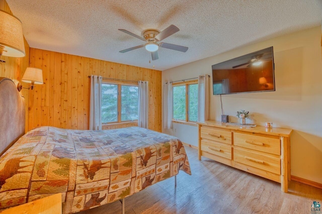 bedroom with a textured ceiling, ceiling fan, hardwood / wood-style floors, and wooden walls