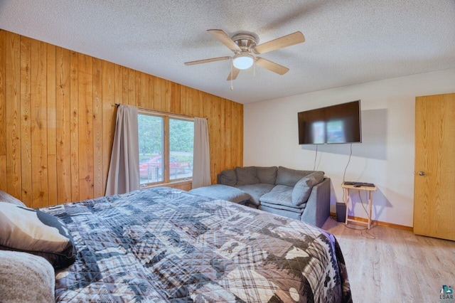 bedroom featuring ceiling fan, a textured ceiling, light wood-type flooring, and wooden walls