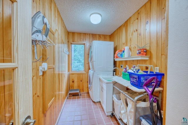 laundry area with a textured ceiling, light tile patterned floors, stacked washer / drying machine, and wood walls